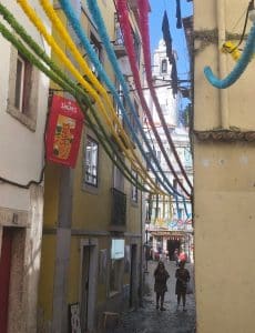 Colorful festival decorations hanging above a narrow street in Alfama, Lisbon.